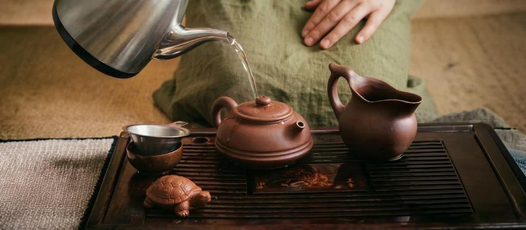Hot water is poured in a circular motion into and over a gaiwan or Yixing teapot to warm the teaware, after which the water from the pot is poured into a fairness pitcher.